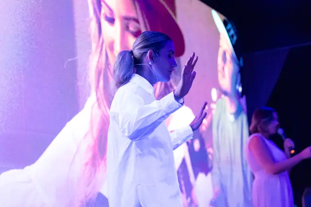 Condutora do momento de fé, de olhos fechados e mãos erguidas no palco, com a cantora ao fundo