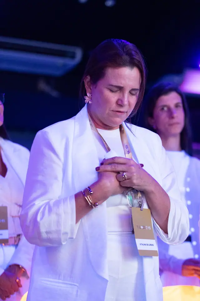 Participante de olhos fechados, com as mãos unidas junto ao peito, em oração