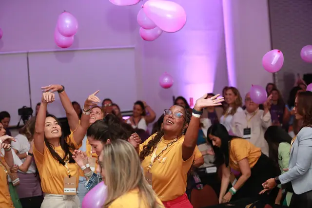 Participantes dançando sob luz rosa, com balões ao fundo