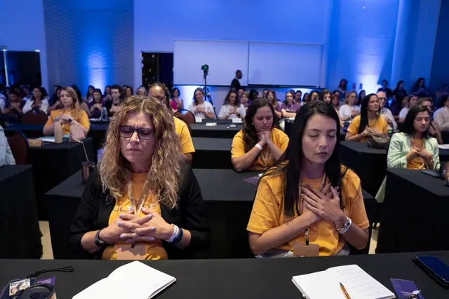 Participantes de olhos fechados, com as mãos no peito, em um momento de reflexão